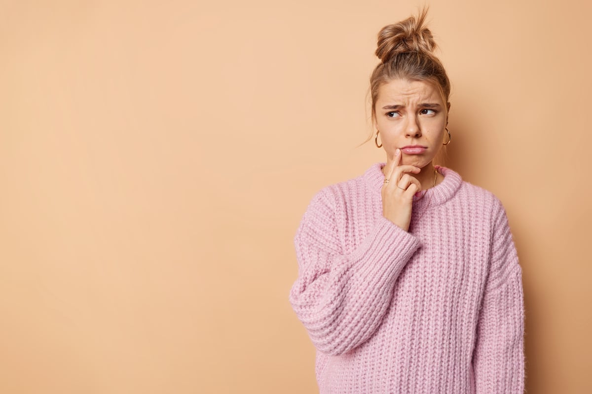 horizontale-aufnahme-einer-unzufriedenen-traurigen-frau-mit-den-lippen-sieht-ungluecklich-weg-traegt-lockere-strickpullover-posen-vor-beigem-hintergrund-mit-kopienraum-auf-der-linken-seite-damit-ihre-werbung-schlechte-laune-hat